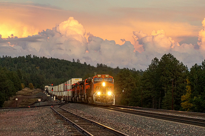 Intermodal container unit train rolls through tree-covered hills at sunset near Parks, Arizona. Intermodal container unit train rolls through tree-covered hills at sunset near Parks, Arizona.
